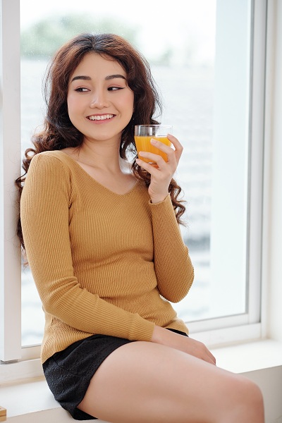 A girl drinking an orange juice by the window