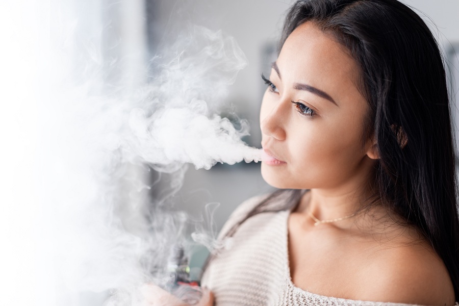 Casual asian woman vaping electronic cigarette at home