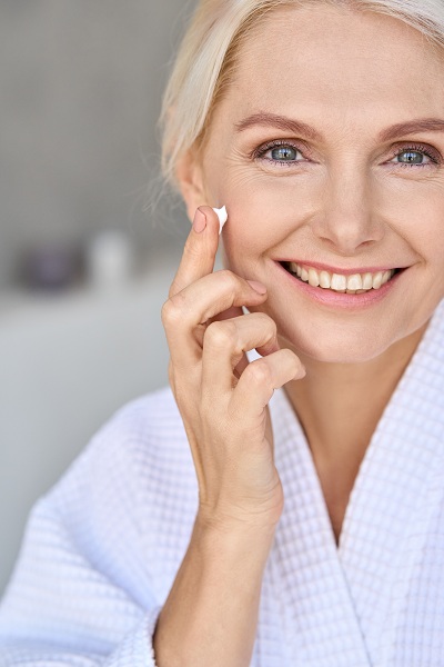 Happy and smiling middle aged woman applying face cream
