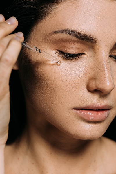 Young woman putting on facial serum for skincare