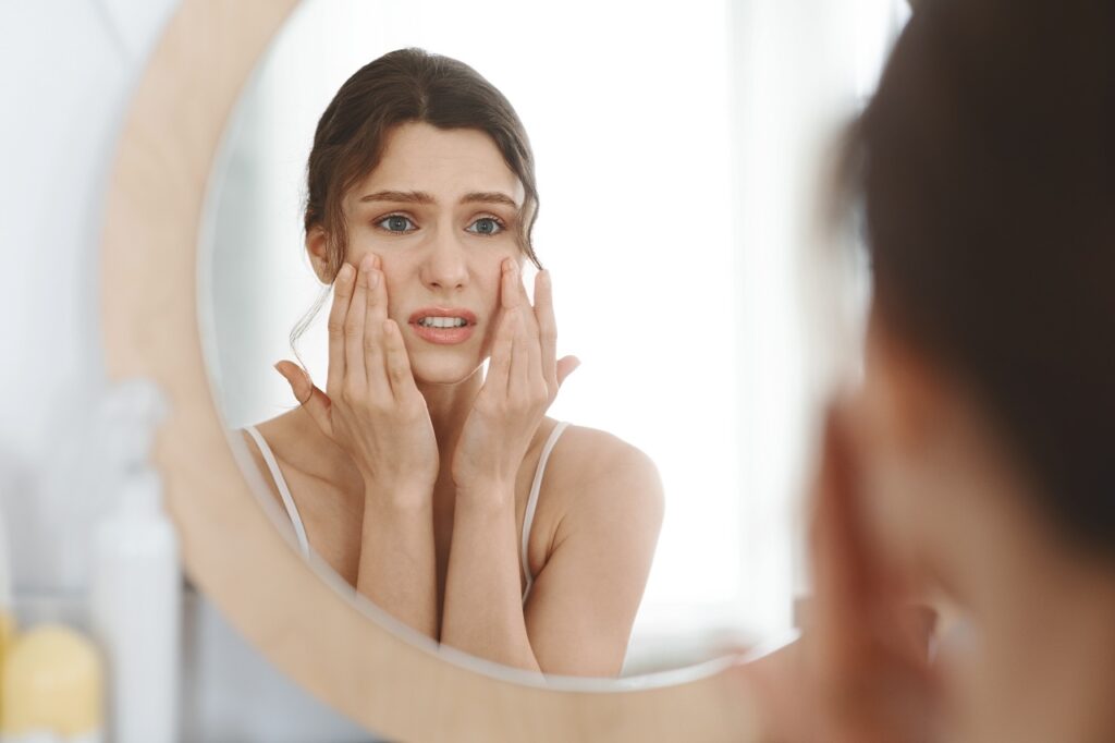 Stressed girl touching her skin and looking at mirror