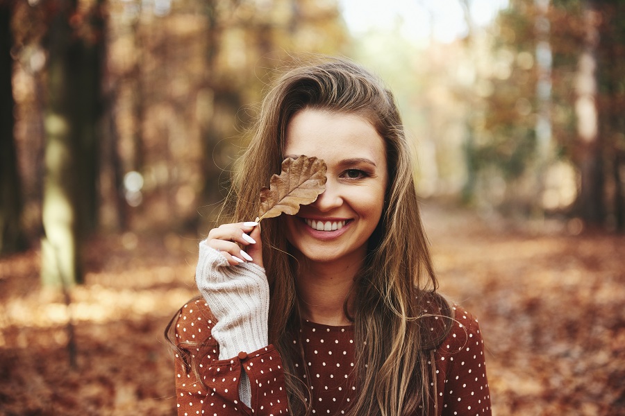 Woman covering eye with autumn leaves