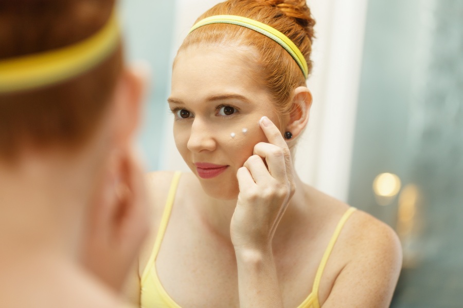 Young Woman Applies Anti-Aging Cream Looking At Mirror