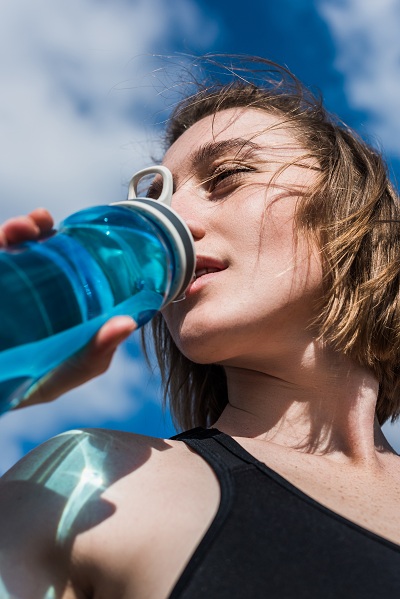 young woman drinking water after workout outdoors